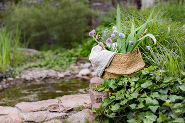 A wicker basket of wildflowers on the rocky shore of a small lake. Landscape design of a private...