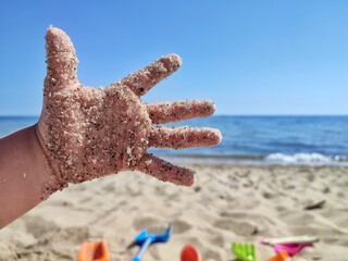 A child's open palm with stuck sand while playing on the beach on a summer day