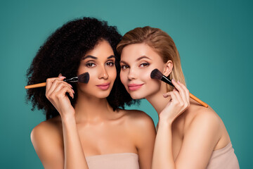 Photo of two attractive girls applying makeover on face with brush isolated cyan color background