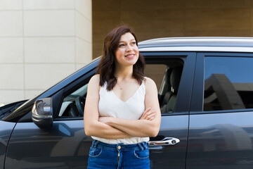 Confident and independent woman leaning against her car, smiling with arms crossed in an urban setting