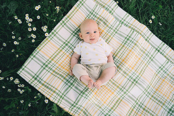 Cute happy baby lying on blanket on green grass at summer outdoors. 3 months old barefoot baby on...