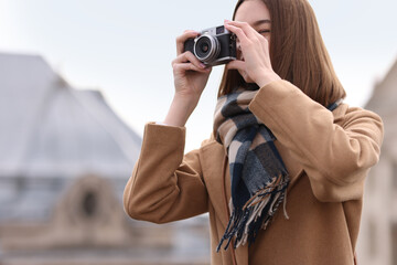 Beautiful woman in warm scarf taking picture with vintage camera outdoors, space for text