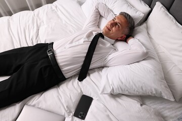 Fototapeta premium Businessman in office wear resting on bed indoors, above view