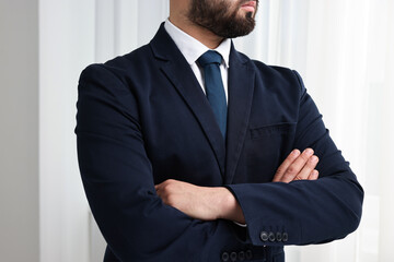 Businessman in suit and necktie with crossed arms indoors, closeup