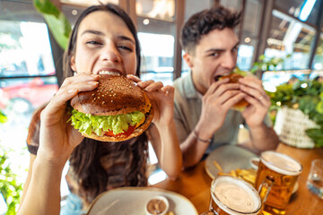 Couple eating fresh burger sitting at pub restaurant table