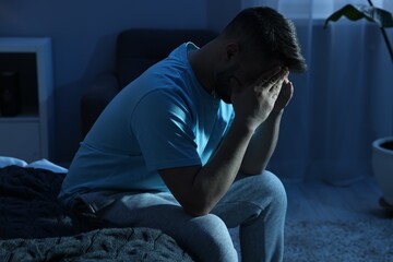 Man covering face with hands on bed at night