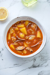 Bowl of manhattan chowder with vongole clams on a white marble background, vertical shot, high angle view