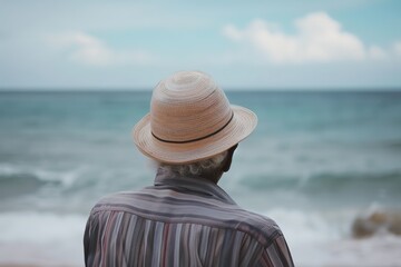 Elderly person gazing at the sea wearing a straw hat.