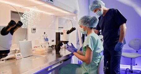Laboratory worker examining samples under microscope in clinic. An embryologist is seen performing artificial fertilization of a human egg using a microscope in a laboratory setting - Powered by Adobe