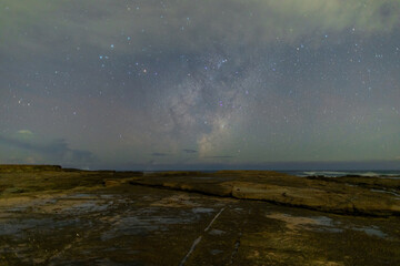 Beautiful milky way galaxy over the rock platform at the coastline.