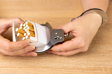 A woman is handcuffed to a pack of cigarettes. Tobacco addiction concept. It's a shame to smoke.