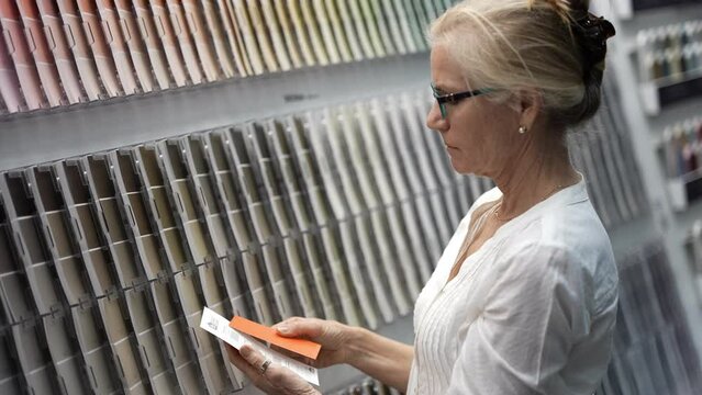 Pretty mature woman looking through paint swatches shopping for home redecorating renovation project, in a hardware store.