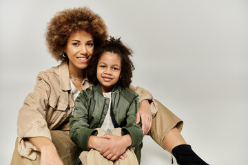 An African American mother and her curly-haired daughter, dressed in stylish clothes, striking a...