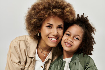 A stylish African American mother with curly afro hair and her little girl posing on a grey...