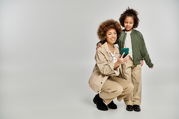 A curly African American mother and daughter in stylish clothes striking a pose together on a grey...