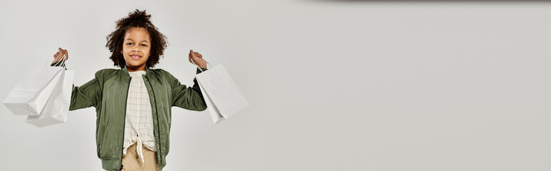A young boy confidently holds shopping bags in front of a white background.