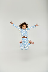 A young African American girl joyfully jumping in the air, wearing blue pajamas
