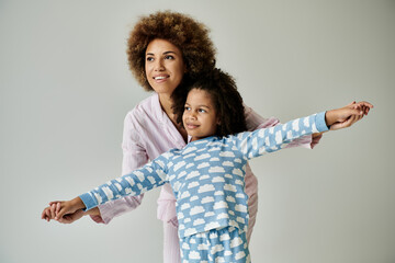 A happy African American mother and daughter in pajamas striking a pose on a grey background.