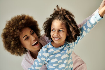 Happy African American mother and daughter in pajamas, enjoying quality time together on a grey...