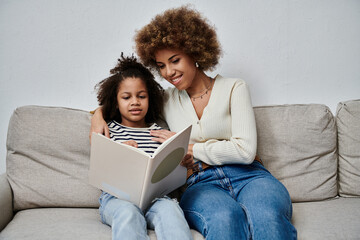 A joyful African American mother and daughter immersed in a captivating book while seated...