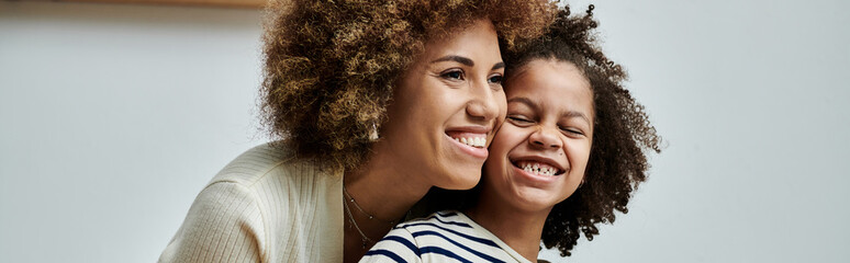 A joyful African American mother and daughter share a heartfelt moment, smiling at each other with...