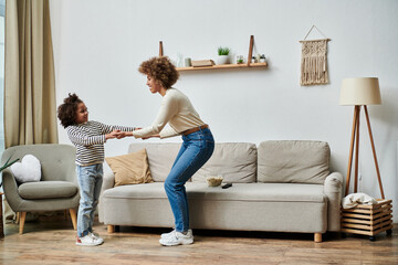 An African American mother and her kid are dancing joyfully in their living room, bonding through...