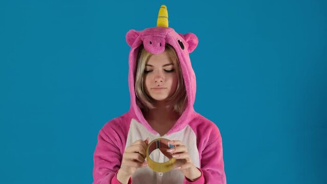 Girl in unicorn pajamas wears hood putting tape on mouth on blue background. Concept of relationship problems with teenagers or parents