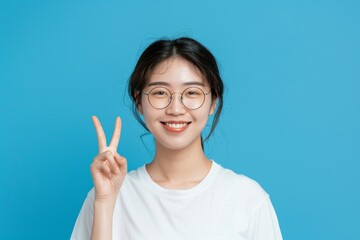 Woman with okay hands or sign for learning success, Certified and Excellence t-shirt on blue studio background. Happy young Asian person in glasses, portrait, and education support emoji.
