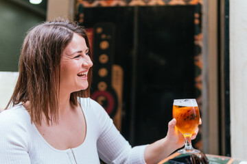 Joyous woman in casual attire raising a glass of beer with a smile