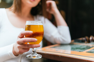 Closeup of a woman in a bar holding a glass of beer, blurred background