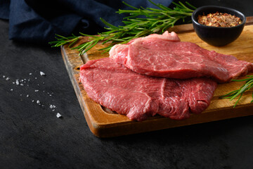Raw marbled steak with rosemary sprig and salt on black background. Copy space. Close up.