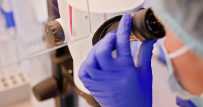 An embryologist conducts artificial fertilization of a human egg using a microscope in a clinical laboratory environment. Embryologist Performing Artificial Fertilization in Laboratory Setting