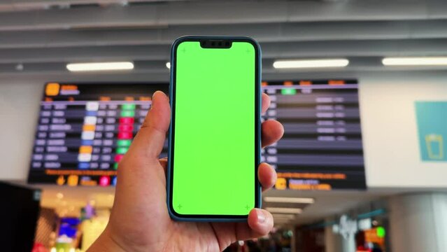 Tourist checking schedule table at the airport terminal and using phone application. Hands with green screen. Close-up technology concept.
