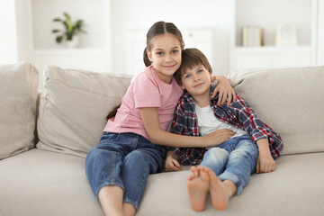 Happy brother and sister spending time together on sofa at home