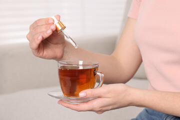 Woman dripping food supplement into cup of tea indoors, closeup