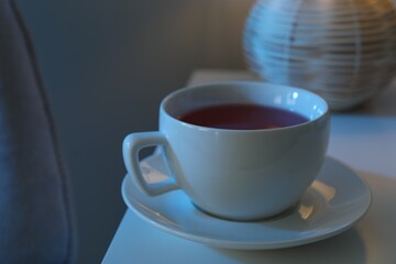Cup of hot tea and nightlight on white table at night, closeup