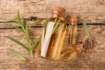 Aromatic essential oils in bottles and rosemary on wooden table, flat lay