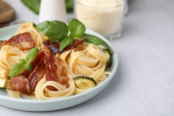 Tasty pasta with bacon and basil on light grey table, space for text