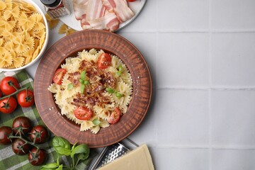 Tasty pasta with bacon, tomatoes and basil on white tiled table, flat lay. Space for text