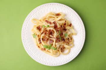 Tasty pasta with bacon and basil on light green table, top view