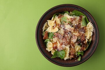 Tasty pasta with bacon and basil on light green table, top view. Space for text