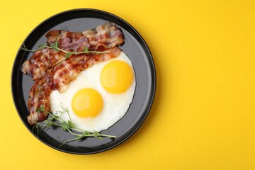 Fried eggs, bacon and microgreens on yellow background, top view. Space for text