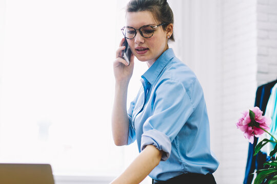 Manager organizing working schedule of showroom on telephone sitting on sewing table.Creative dressmaker talking on smartphone with designer to preparing collection for fashion industry event