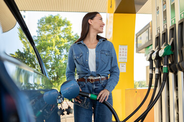 Happy European lady refueling her car at modern petrol station outdoor, female driver standing near...