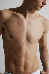 Fototapeta premium Cropped image of shirtless young guy posing isolated on grey studio background. Perfect muscular body shape. Perfect body shape. Concept of male beauty, body care, fitness, sport, health