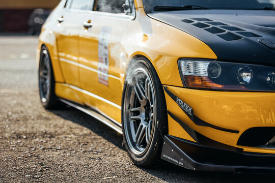 Yellow Milsubishi Lancer evolution at local track driving event with smoke coming out of the front wheel arches. Evo IX Smoking brakes after few hot laps on time attack. Chaiky, Ukraine - July 20 2014