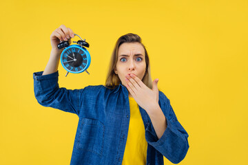 Young sad shocked woman hold alarm clock isolated on yellow background studio. Bad mood night nap...