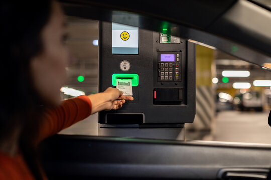 Woman driving into underground parking garage and collecting ticket from car park automated machine, rear view