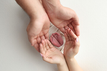 The palms of the father, the mother are holding the foot of the newborn baby in a white blanket....