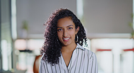 Indian close up of curly hair young adult gen z boss woman owner lady face standing proud look cam indoor day office happy expert teen girl female agent staff do pose head shot video job work place